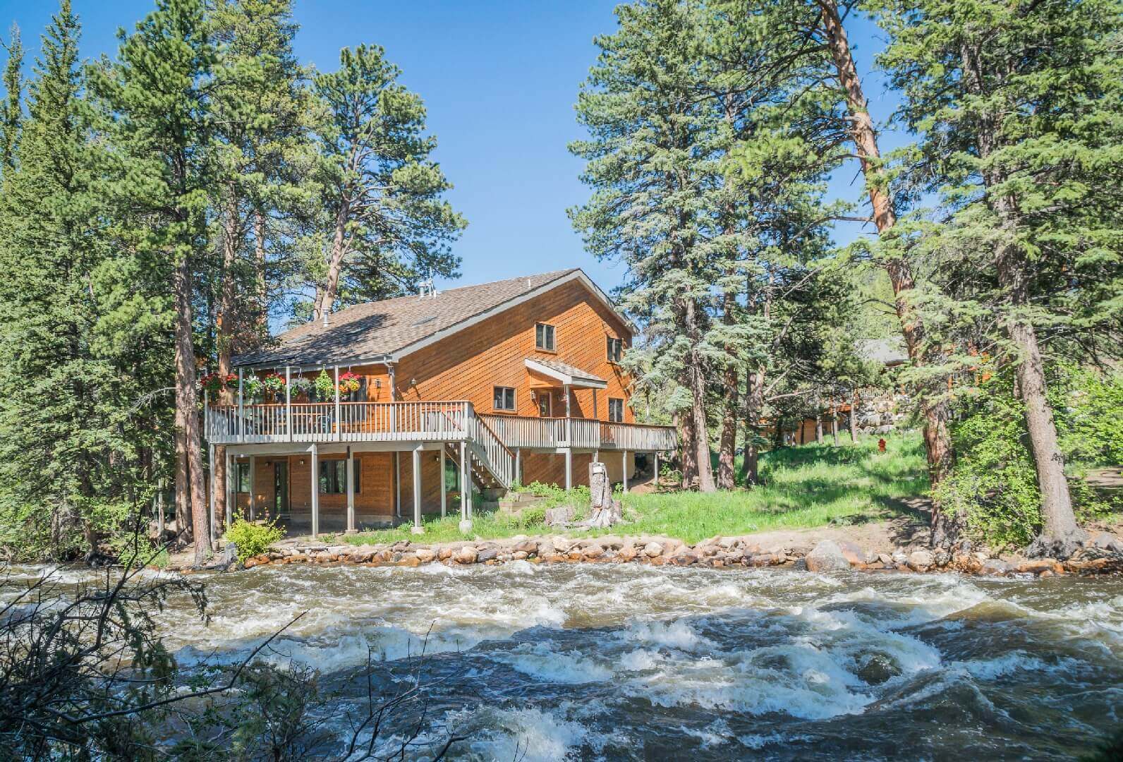 Lodge with deck beside flowing river and trees